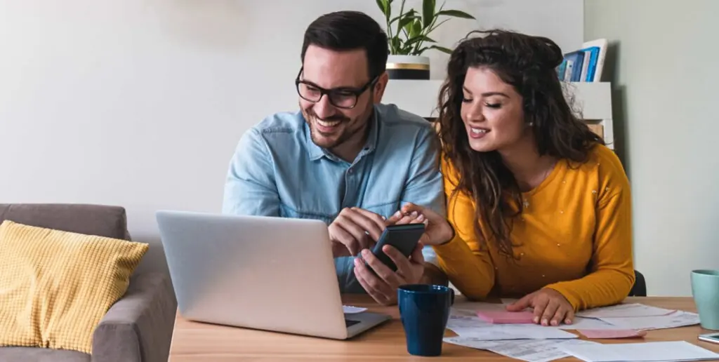 Define a Budget - Inspire Homes Couple happily managing finances on laptop together.
