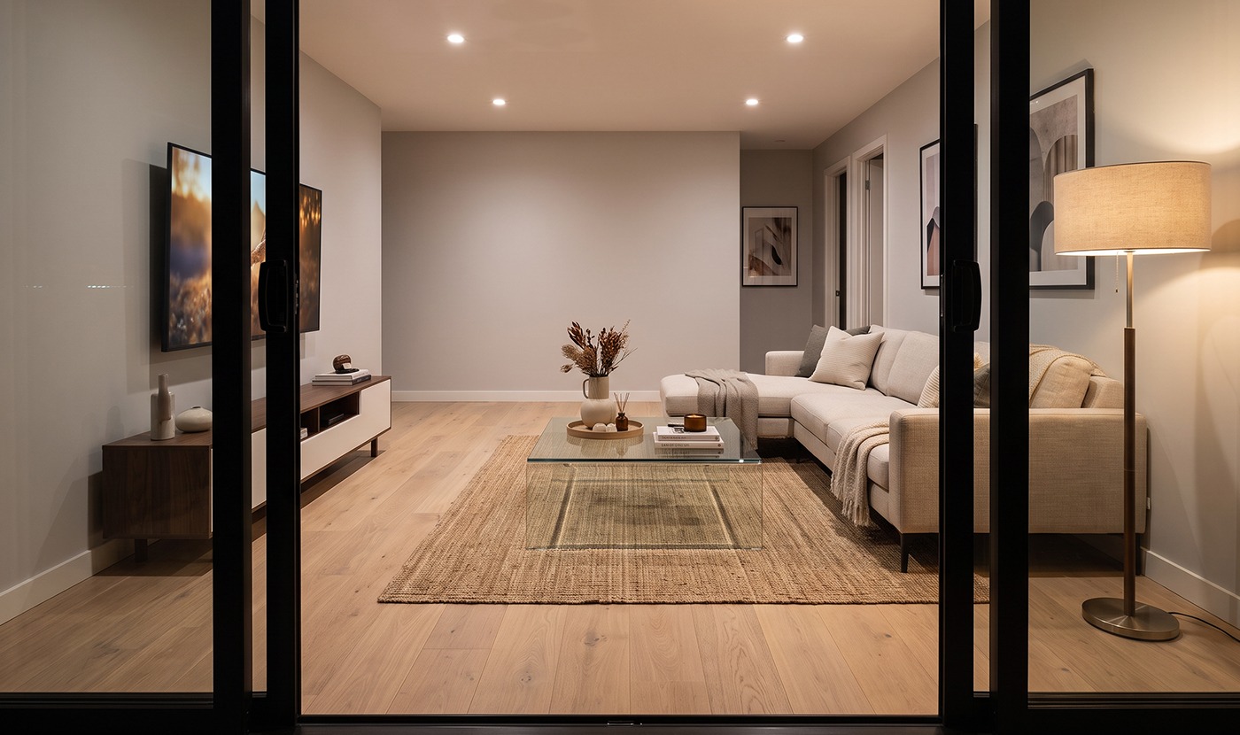 Modern living room with a beige sectional, glass coffee table, and TV on a wooden console seen through glass doors at dusk lighting.
