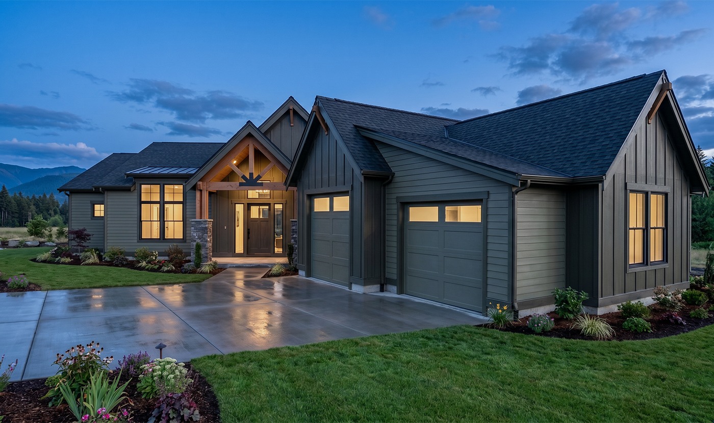 Modern gray house with a three-car garage at dusk, warm entry lights, and a landscaped front yard.