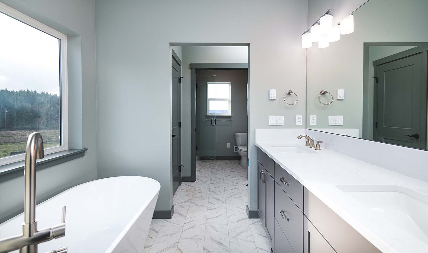 Modern bathroom with a double-sink vanity, white countertops, gray cabinets, and a tub by a large window.