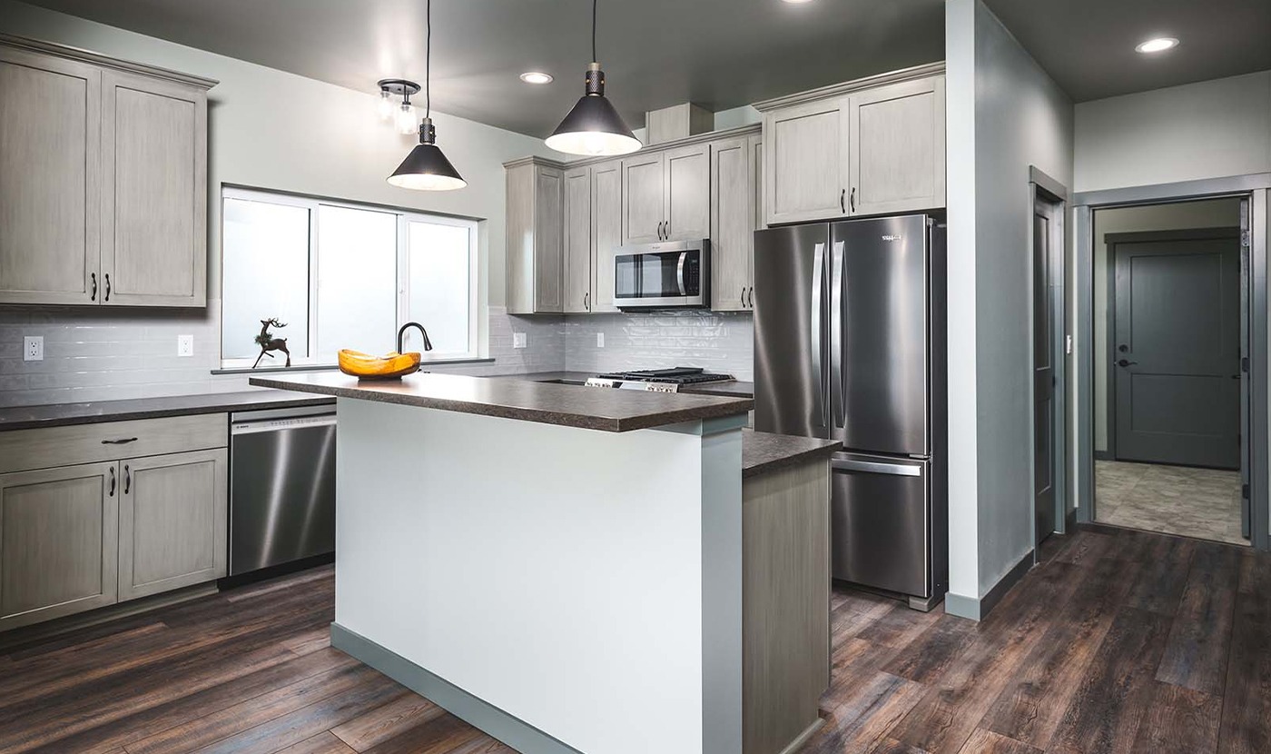 Modern kitchen with grey cabinets, stainless steel fridge and dishwasher, and a central island.
