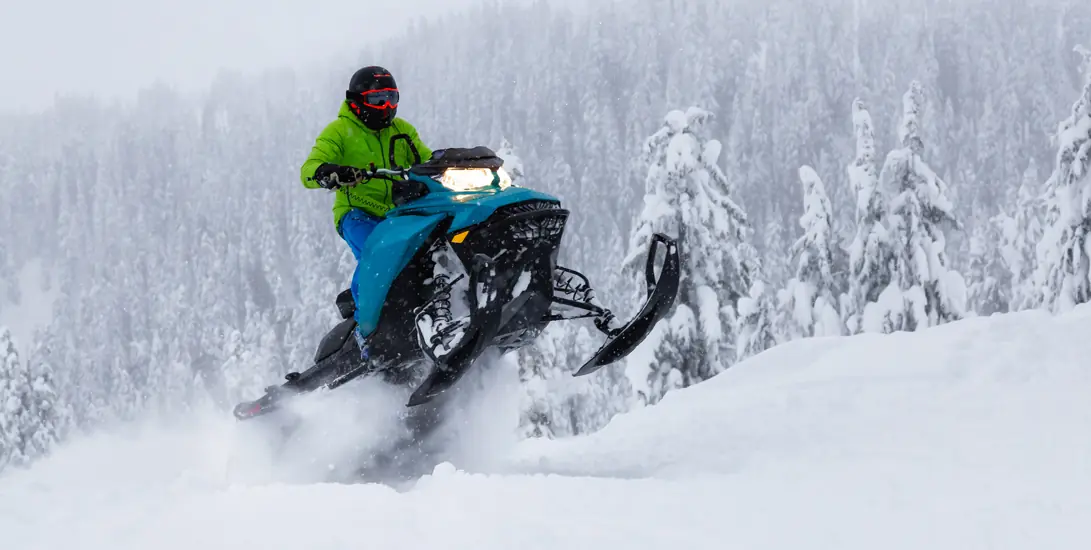 Snowmobile rider navigating through snowy forest terrain
